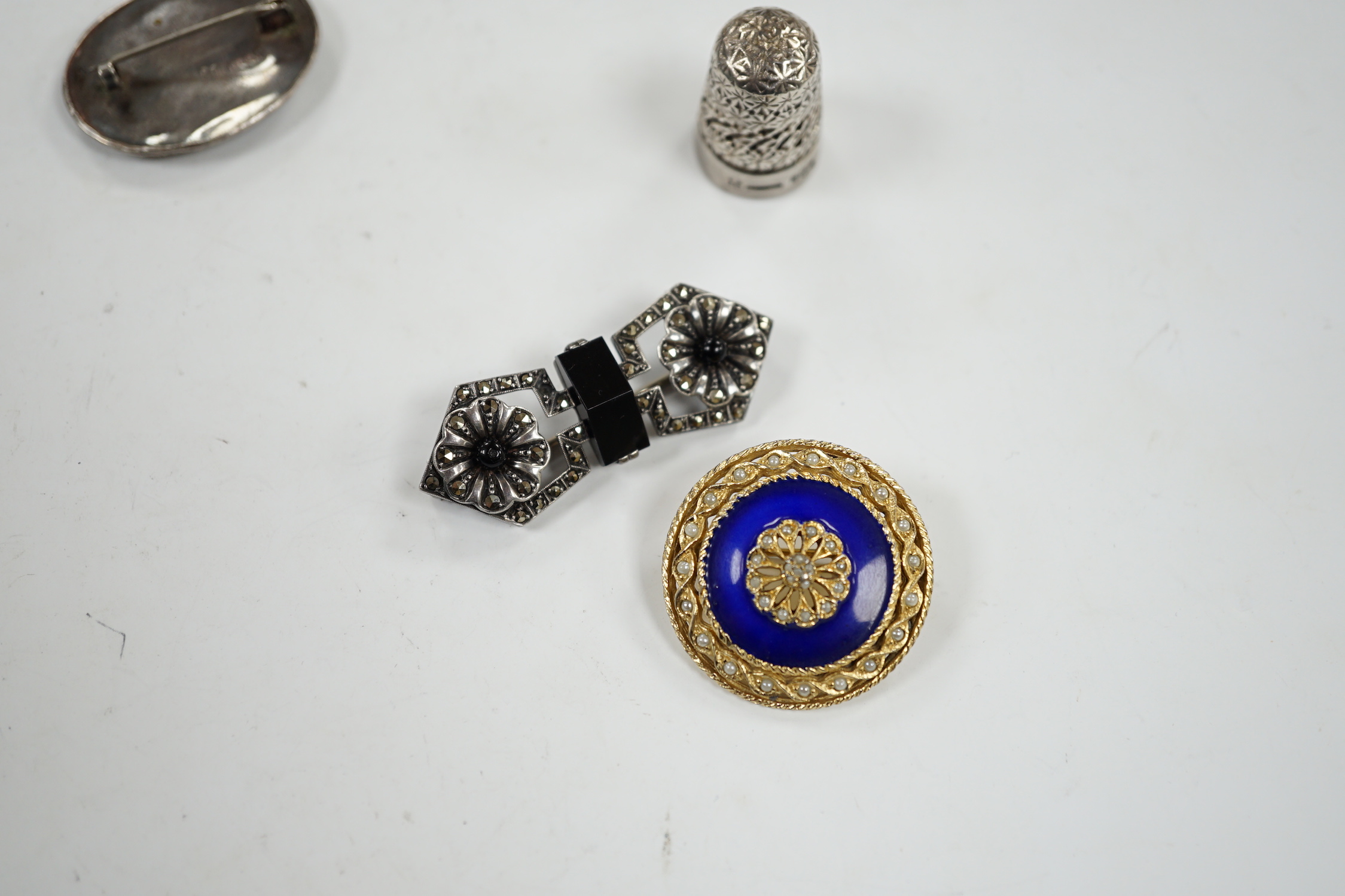 A George V silver thimble, a later silver brooch, a white metal, marcasite and black onyx brooch and one other brooch.